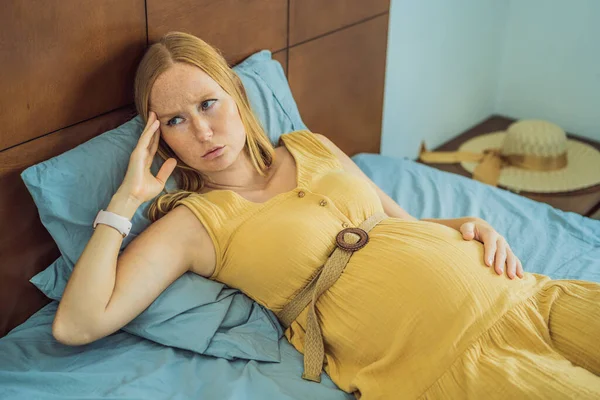 A stressed tired pregnant mother lying in bed at home. Morning sickness and nausea.