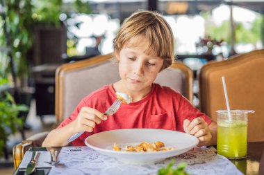 Güneşli bir günde lokantada tek başına yemek yiyen beyaz bir çocuğun portresi. Sağlıklı beslenme kavramı..