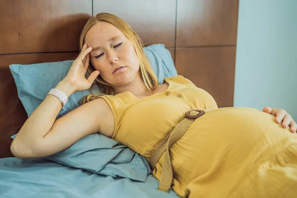 A stressed tired pregnant mother lying in bed at home. Morning sickness and nausea.