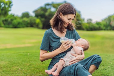 Anne parkta süt şişesinden bebeği tutuyor ve besliyor. Annesi tarafından şişeyle beslenen sevimli bir bebeğin portresi. Sevgi dolu kadın oğluna süt veriyor..