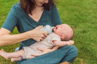 Anne parkta süt şişesinden bebeği tutuyor ve besliyor. Annesi tarafından şişeyle beslenen sevimli bir bebeğin portresi. Sevgi dolu kadın oğluna süt veriyor..