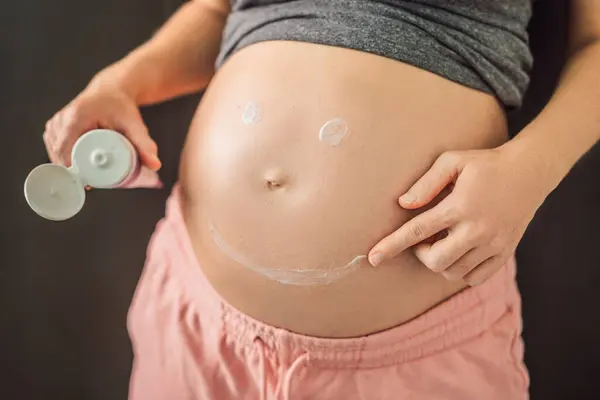 彼女の大きな腫れ 女性の腹に腹バターを塗る快適なホームウェアで肯定的な若い妊婦 — ストック写真
