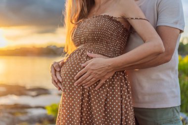 40 yaşını geçmiş mutlu, olgun bir çift, günbatımında sakin bir şekilde yürüyüşten zevk alıyor. Neşeleri, hamileliklerinin ilerleyen dönemlerindeki yolculuklarına kucak açıyorlar..
