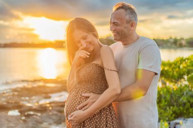 40 yaşını geçmiş mutlu, olgun bir çift, günbatımında sakin bir şekilde yürüyüşten zevk alıyor. Neşeleri, hamileliklerinin ilerleyen dönemlerindeki yolculuklarına kucak açıyorlar..