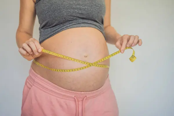 Young woman measuring her pregnant belly with centimeter tape. Centimeters European standard. Preparation for childbirth, Girl big belly advanced healthy pregnancy.