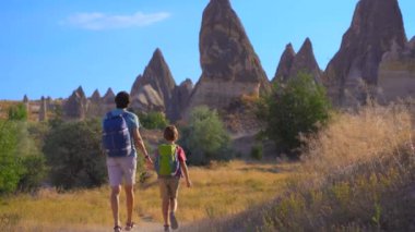 Genç adam ve oğlu turistler, doğa sanatının farklı şekilli kayalardan oluşan gerçeküstü bir manzara oluşturduğu Türkiye 'nin Kapadokya kentindeki Aşk Vadisi' ni ziyaret ediyorlar. Bu eşsiz oluşumlar,