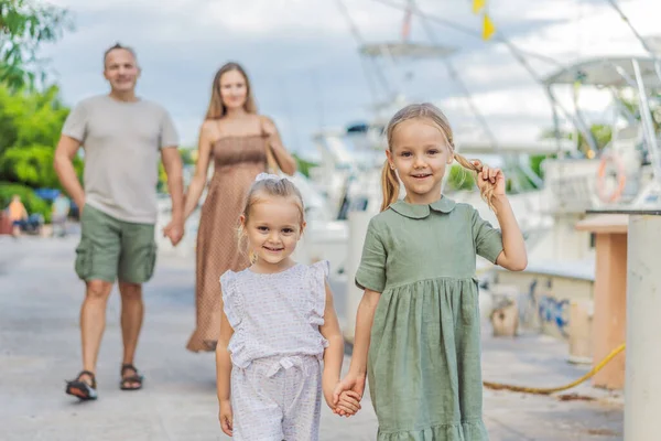 A happy, mature couple over 40 with their two daughters enjoying a leisurely walk on the waterfront, their joy evident as they embrace the journey of pregnancy later in life.