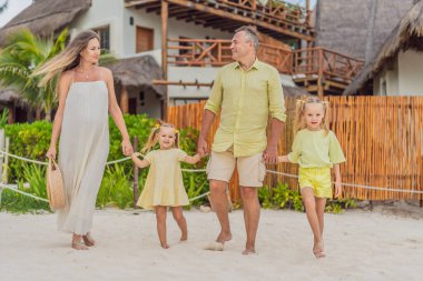 Neşeli bir aile, iki kız, baba ve hamile bir anne, tropik plaj saadeti içinde güneşleniyorlar, cennetin ortasında ışıl ışıl bir hamileliği kutluyorlar..