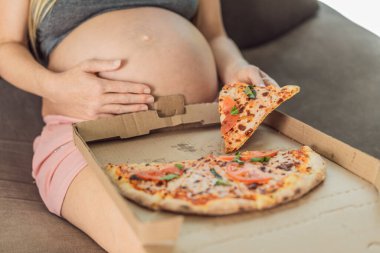 Hamile bir kadın bir dilim pizzanın tadını çıkarırken aynı zamanda zevkli ve rahatlatıcı bir zevke hasret. Heyecanlı Hamile Genç Bayan Pizza Tutma Isırmanın tadını çıkarıyor