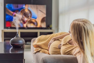 Mutlu, hamile bir kadın, rahatlatıcı aromasının tadını çıkarırken aynı zamanda rahatlatıcı bir TV videosunun tadını çıkarıyor. Hamile yolculuğu boyunca sakinliğini kucaklıyor..