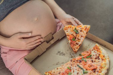 Hamile bir kadın bir dilim pizzanın tadını çıkarırken aynı zamanda zevkli ve rahatlatıcı bir zevke hasret. Heyecanlı Hamile Genç Bayan Pizza Tutma Isırmanın tadını çıkarıyor