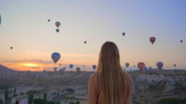 Kapadokya, Türkiye 'de sıcak hava balonlarına bakan turist kadın. İyi yolculuklar hindi konsepti. Dağın tepesinde harika manzaranın tadını çıkaran bir kadın