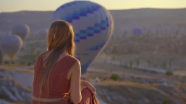 Kapadokya, Türkiye 'de sıcak hava balonlarına bakan turist kadın. İyi yolculuklar hindi konsepti. Dağın tepesinde harika manzaranın tadını çıkaran bir kadın