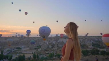 Kapadokya, Türkiye 'de sıcak hava balonlarına bakan turist kadın. İyi yolculuklar hindi konsepti. Dağın tepesinde harika manzaranın tadını çıkaran bir kadın
