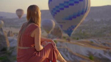 Kapadokya, Türkiye 'de sıcak hava balonlarına bakan turist kadın. İyi yolculuklar hindi konsepti. Dağın tepesinde harika manzaranın tadını çıkaran bir kadın