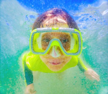 Dalgaların altında bir çocuk dalış maskesiyle derinlere dalıyor ve sualtı dünyasının harikalarını keşfediyor..