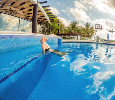 Su sporunu kucaklayan hamile bir kadın, su altı aerobiğinde güç ve dinginlik gösteriyor. Havuzda dingin ve güçlü bir görüntü yaratıyor..