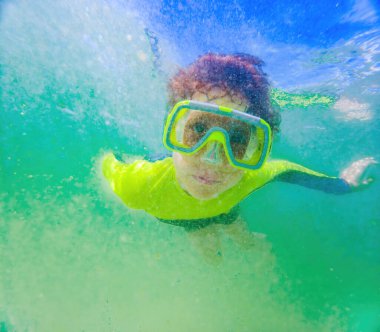 Dalgaların altında bir çocuk dalış maskesiyle derinlere dalıyor ve sualtı dünyasının harikalarını keşfediyor..