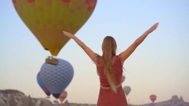 Kapadokya, Türkiye 'de sıcak hava balonlarına bakan turist kadın. İyi yolculuklar hindi konsepti. Dağın tepesinde harika manzaranın tadını çıkaran bir kadın