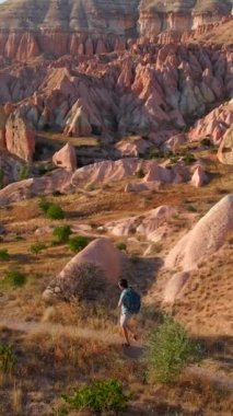 Dikey video. Kapadokya, Goreme yakınlarındaki Kızıl ya da Pembe Vadi 'de bir turist yürüyüş yapıyor. Sıcak tonlarda boyanmış manzara, eşsiz jeolojik oluşumları ve peri bacalarını gözler önüne seriyor.