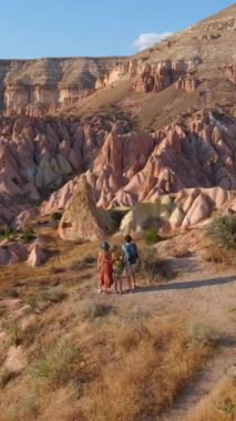 Dikey video. Kapadokya, Goreme yakınlarındaki Kızıl ya da Pembe Vadi 'de bir turist ailesi yürüyüş yapıyor. Sıcak tonlarda boyanmış manzara, eşsiz jeolojik oluşumları ve peri bacalarını gözler önüne seriyor.