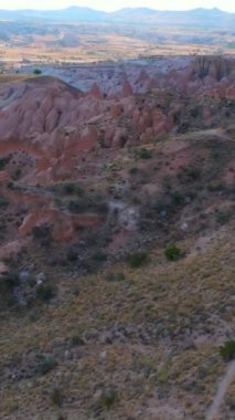 Dikey video. Kapadokya yakınlarındaki Kızıl ya da Pembe Vadi 'nin büyüleyici tonlarını bu büyüleyici hava fotoğrafında tecrübe edin. Manzara, sıcak tonlarda resmedilmiş, benzersiz