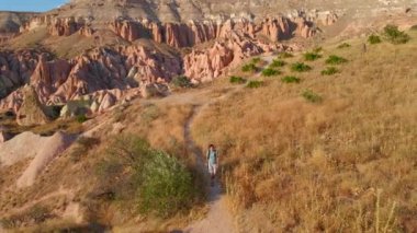 Kapadokya, Goreme yakınlarındaki Kızıl ya da Pembe Vadi 'de bir turist yürüyüş yapıyor. Sıcak tonlarda boyanmış manzara, bölgeyi tanımlayan eşsiz jeolojik oluşumları ve peri bacalarını gözler önüne seriyor.