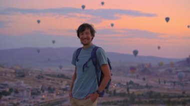 Genç bir turist Kapadokya, Türkiye 'de sıcak hava balonlarına bakıyor. İyi yolculuklar hindi konsepti. Dağın tepesinde harika manzaranın tadını çıkaran bir adam.