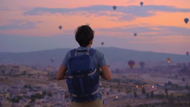 在土耳其的卡帕多西亚 一位年轻的游客正在看热气球 土耳其旅途愉快的概念 一个人在山顶上欣赏美丽的风景 — 图库视频影像