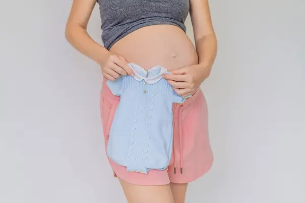 柔らかい瞬間 妊娠中の母親は 母性の喜びを期待して 彼女の成長する腹に対して赤ちゃんの服を締め付ける — ストック写真