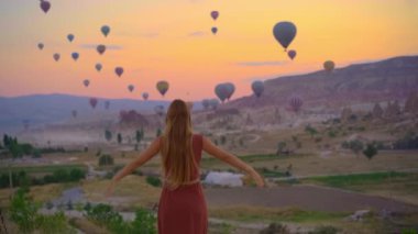 Kapadokya, Türkiye 'de genç bir kadın sıcak hava balonlarına bakıyor. İyi yolculuklar hindi konsepti. Dağın tepesindeki kadın harika manzaranın tadını çıkarıyor.