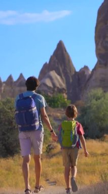 Dikey video. Genç adam ve oğlu turistler, doğa sanatının farklı şekilli kayalardan oluşan gerçeküstü bir manzara oluşturduğu Türkiye 'nin Kapadokya kentindeki Aşk Vadisi' ni ziyaret ediyorlar. Bu eşsiz oluşumlar