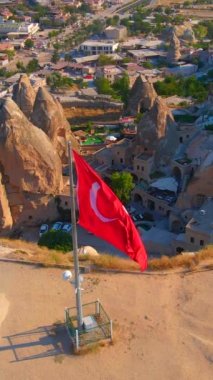 Dikey video. Goreme, Cappadocia, Türkiye 'nin havadan çekilmiş videosu. Goreme tepesinin tepesinde Türk Cumhuriyeti 'ne ait el sallayan bir bayrak bulunmaktadır..