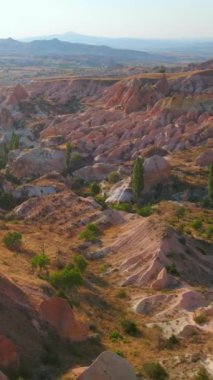 Dikey video. Kapadokya yakınlarındaki Kızıl ya da Pembe Vadi 'nin büyüleyici tonlarını bu büyüleyici hava fotoğrafında tecrübe edin. Manzara, sıcak tonlarda resmedilmiş, benzersiz