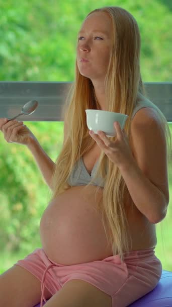 Сияющая Беременная Женщина Наслаждается Питательным Моментом Сидя Фитболе Наслаждаясь Миской — стоковое видео