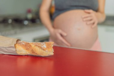 Hamile bir kadın mutfakta ekmek yiyor. Hamilelik süresince glütenin etkisini araştırmak: anne sağlığı ve fetal gelişim için potansiyel faydaları ve riskleri anlamak.