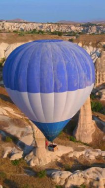 Dikey hava görüntüsü. Kapadokyaca gökyüzünün tuvaline yansıyan bu video, sıcak hava balonu festivalinin büyüleyici görüntüsünü sergiliyor. Mavi bir balon zarif bir şekilde süzülüyor