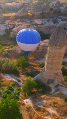 Dikey hava görüntüsü. Kapadokyaca gökyüzünün tuvaline yansıyan bu video, sıcak hava balonu festivalinin büyüleyici görüntüsünü sergiliyor. Mavi bir balon zarif bir şekilde süzülüyor