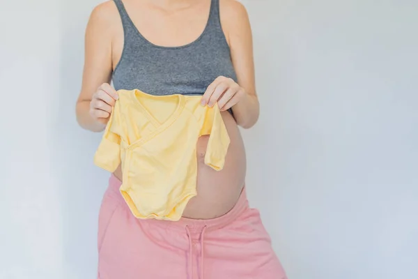 予想の柔らかい瞬間 妊娠中の女性は彼女の手で彼女の生まれていない赤ちゃんの服を粉砕し 小さな子供の到着の準備の甘さを味わいます — ストック写真