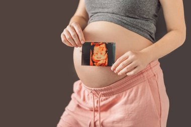 Expectant mother tenderly connects with her unborn child, holding ultrasound photo to her pregnant belly. clipart