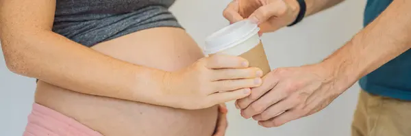 Husband forbids pregnant wife to drink coffee. A pregnant woman holds a cup of coffee in her hands. Caffeine safety, myths about coffee during pregnancy concept. BANNER, LONG FORMAT