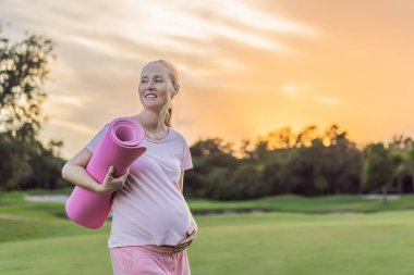 Enerjik hamile kadın dışarıda egzersiz yapıyor, dinlendirici ve sağlık bilinci açık hava egzersizi için bir paspas kullanıyor..