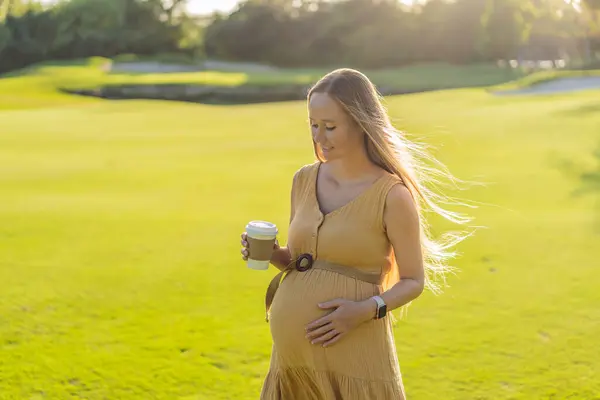 妊娠中の女性は屋外でコーヒーを楽しんでおり 妊娠中の飲料の快適な暖かさで自然のシンプルな喜びを融合させています — ストック写真