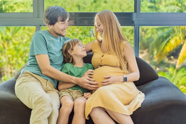 stock image Cozy family time at home as pregnant mom, dad, and son enjoy shared moments on the sofa, creating heartwarming memories and cherishing their time together.