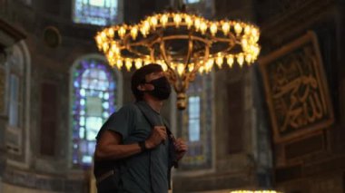 Yüz maskesi takan bir erkek turist, tapınakların görkemli güzelliğine dalmış, İstanbullar Ayasofya 'nın kutsanmış güzelliği içinde huşu içinde duruyor. Yavaş çekim videosu