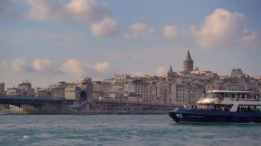 5.05.2021 - ISTANBUL, TURKEY: Istanbuls ikonik Galata Kulesi 'nin çarpıcı bir görüntüsü, şehrin silueti üzerinde görkemli bir şekilde yükseliyor. Ön planda bir sürü insan, tekne ve martı var.