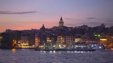 Alacakaranlıkta tekneyle sakin bir yolculuk İstanbullar 'ın ikonik Galata Kulesi' nin çarpıcı bir görüntüsünü sunuyor. Şehrin ufuk çizgisi üzerinde görkemli bir şekilde yükseliyor.