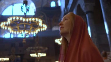 Kafası atkıya sarılı bir kadın turist, tapınakların görkemli ihtişamına dalmış, Ayasofya İstanbullarının kutsanmış güzelliği içinde huşu içinde duruyor. Yavaş çekim videosu