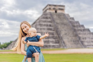 Beautiful tourist woman and her son baby observing the old pyramid and temple of the castle of the Mayan architecture known as Chichen Itza. These are the ruins of this ancient pre-columbian clipart