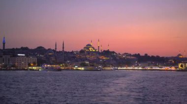 Günbatımında, bir feribot İstanbul 'un tarihi kent merkezine huzurlu bir bakış açısı sunuyor, solan güneş ışığı eski yapıları sıcak bir ışıltıyla yıkıyor.